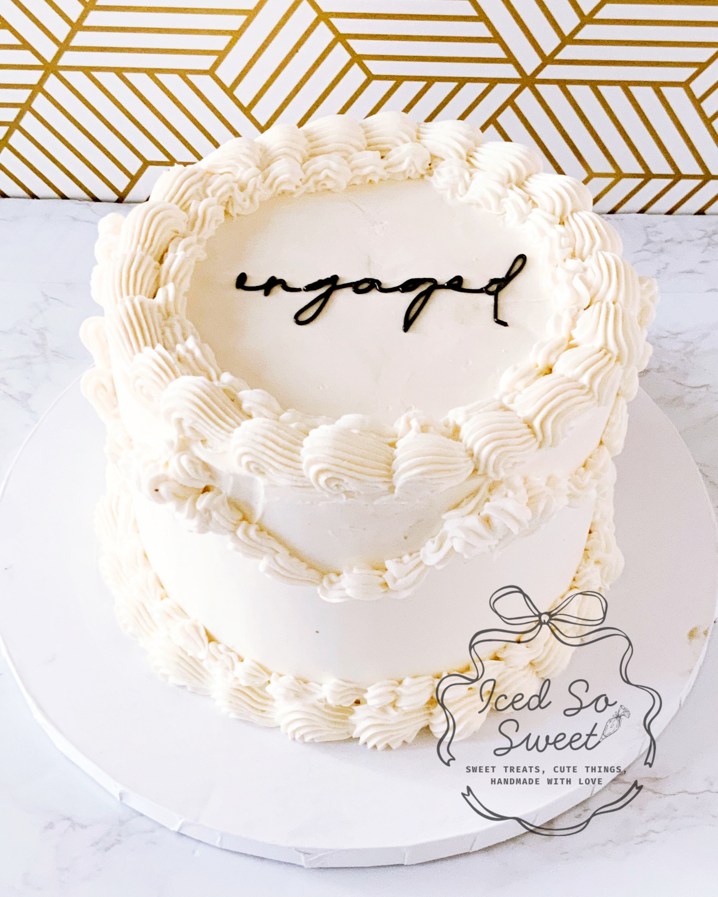 White cake with 'engaged' decoration on a marble surface with gold geometric pattern