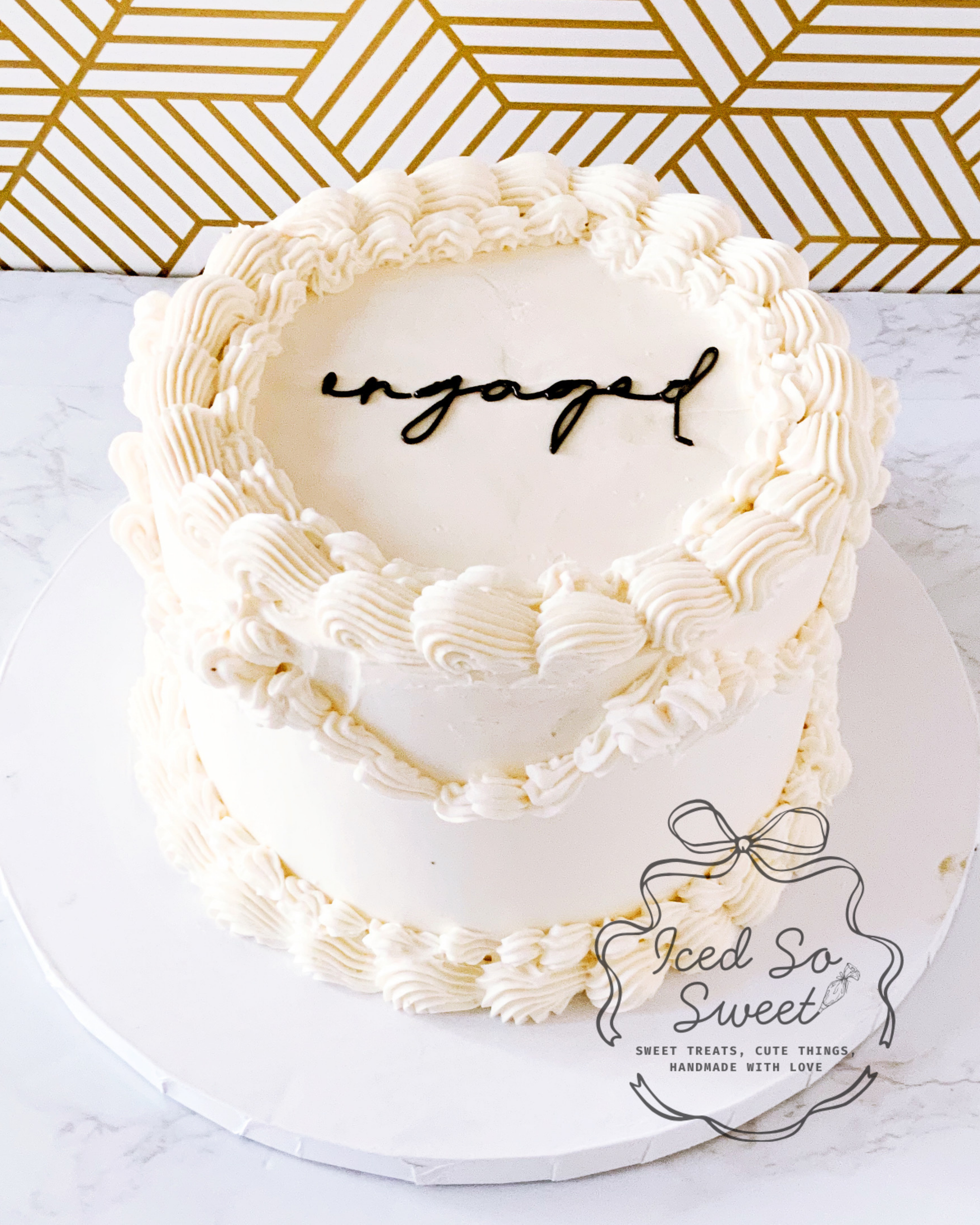 White cake with 'engaged' decoration on a marble surface with gold geometric pattern